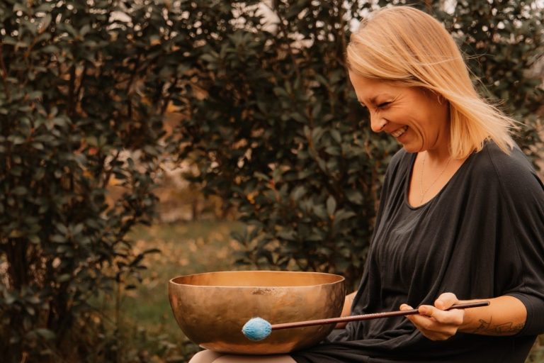 Therapie mit Klangschalen: Klangreisen in der Gruppe; Jessica Fettig sitzt in der Natur und spielt eine Klangschale