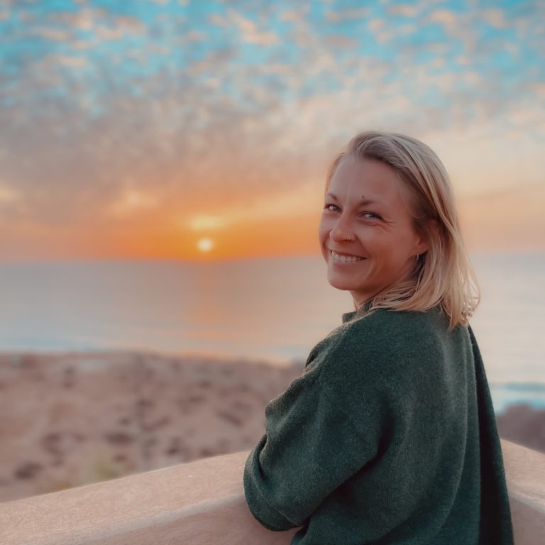 Achtsamkeit lernen zur Persönlichkeitsentwicklung: Jessica Fettig-Soave von achtklang lächelt vor einem idyllischen Sonnenuntergang.