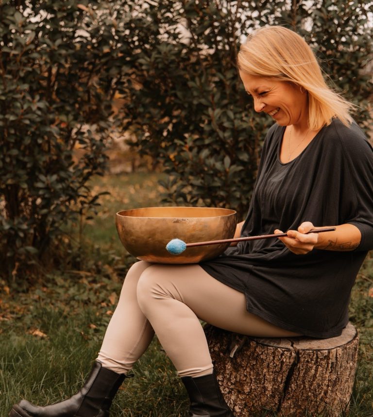 Natur- und Achtsamkeitstraining: Jessica Fettig von achtklang aus Steinmauern spielt lachend eine Klangschale in der Natur